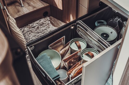 Pull-out kitchen drawer in the Carado motorhome with tableware, storage containers and extra space next to the sink