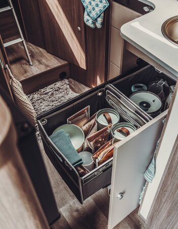 Pull-out kitchen drawer in the Carado motorhome with tableware, storage containers and extra space next to the sink