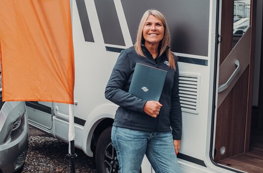 Woman standing in front of an open Carado motorhome next to a Carado flag