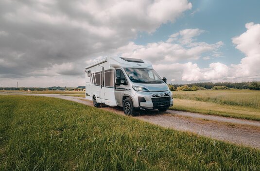Carado motorhome on a country lane in a rural landscape, front and side view under a cloudy sky