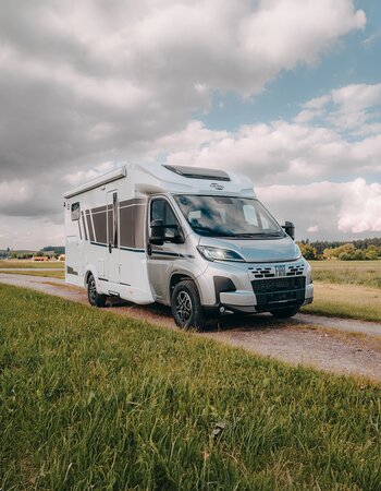 Carado motorhome on a country lane in a rural landscape, front and side view under a cloudy sky