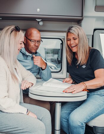 Three people at the table inside a Carado motorhome, looking through documents together