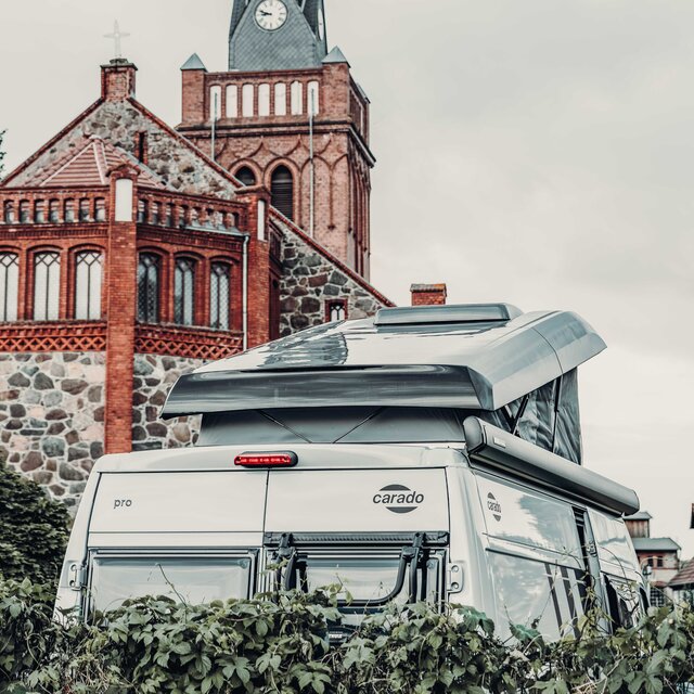 Heckansicht eines Carado Campervan mit aufgeklapptem Aufstelldach vor einer Backsteinkirche