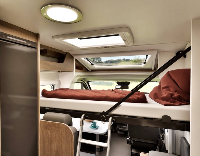 Carado motorhome interior with drop-down bed above the driver’s cab, ladder, roof vent and refrigerator