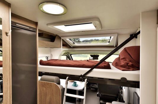 Carado motorhome interior with drop-down bed over the cab, ladder, roof window and refrigerator