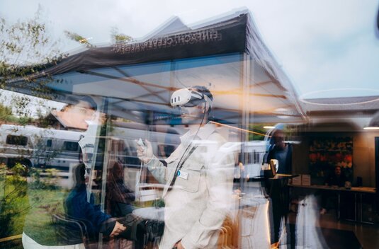 Person wearing VR glasses in an exhibition tent in front of Carado motorhomes