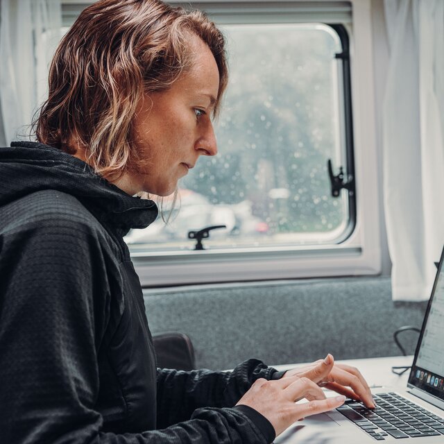 A person works on a laptop inside a Carado motorhome at the table by the window.