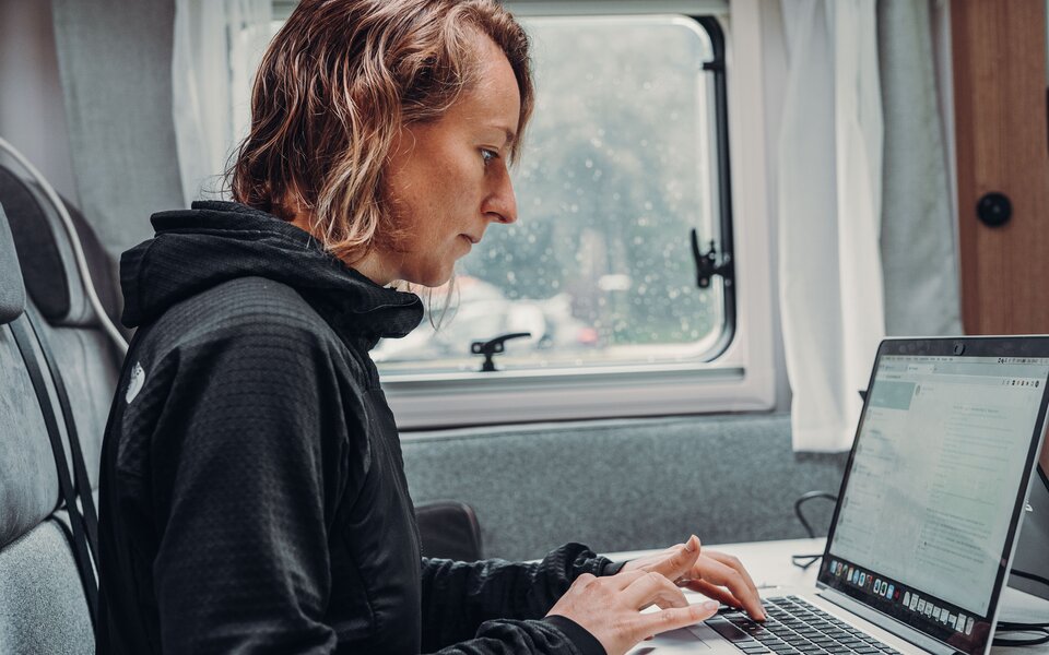A person works on a laptop inside a Carado motorhome at the table by the window.