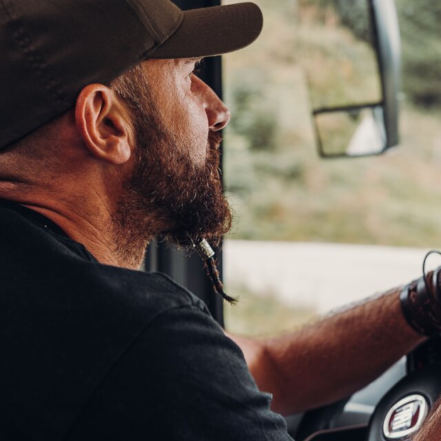 Man with a cap and beard at the wheel of a Carado motorhome, close-up from the driver’s cab