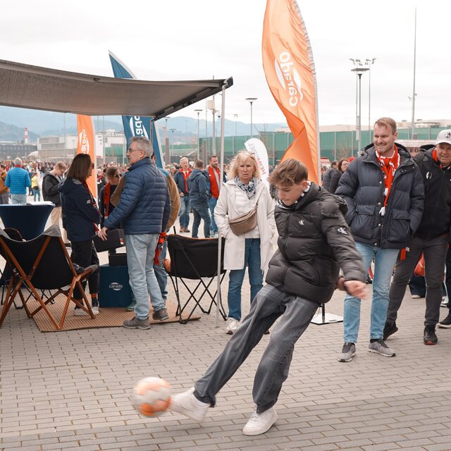 People in front of a Carado camper van at an event site, a teenager kicks a football in front of the open awning