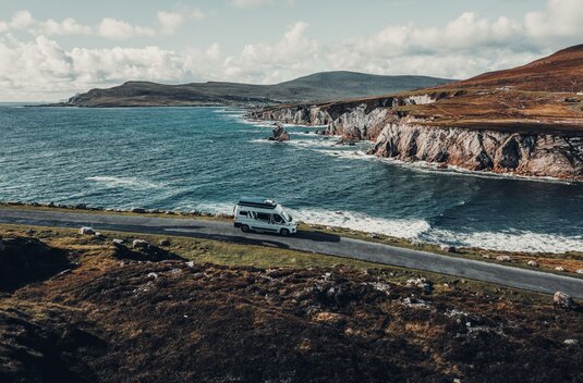 Carado motorhome driving along a coastal road beside steep cliffs by the sea, aerial view
