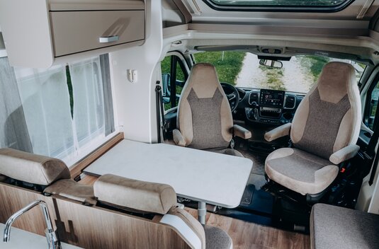 Carado motorhome interior with a seating area, table and swivel driver and passenger seats at the front