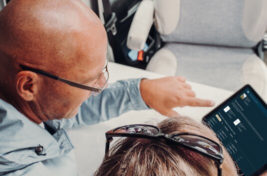 Two people in a Carado motorhome look at a tablet with a booking enquiry at the table