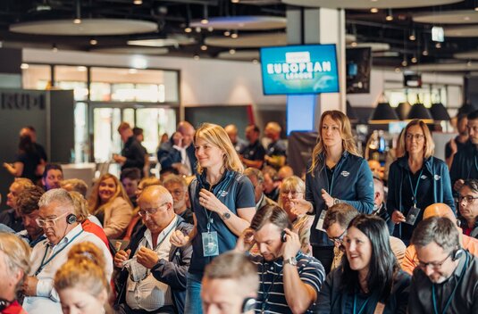 Audience at an indoor event, three Carado employees walking through the rows