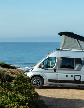 Carado camper van with pop-up roof and bike rack, side view on the coast with a sea view