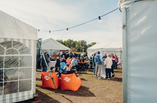 Visitors at a Carado outdoor event between festival tents with seating areas and lounge chairs