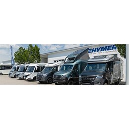 Several Carado motorhomes and camper vans viewed from the front, parked in front of a dealership building on the exhibition grounds
