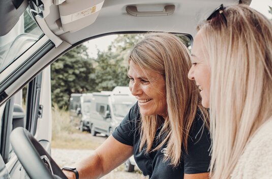 Two women in the cab of a Carado motorhome, with a view of the dashboard and windshield