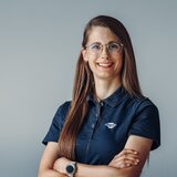 Portrait of a woman wearing a Carado polo shirt and glasses against a grey background