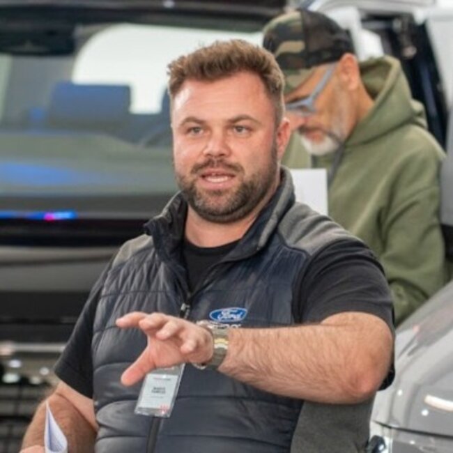 Man with microphone and Ford vest in front of vehicles, second person in the background