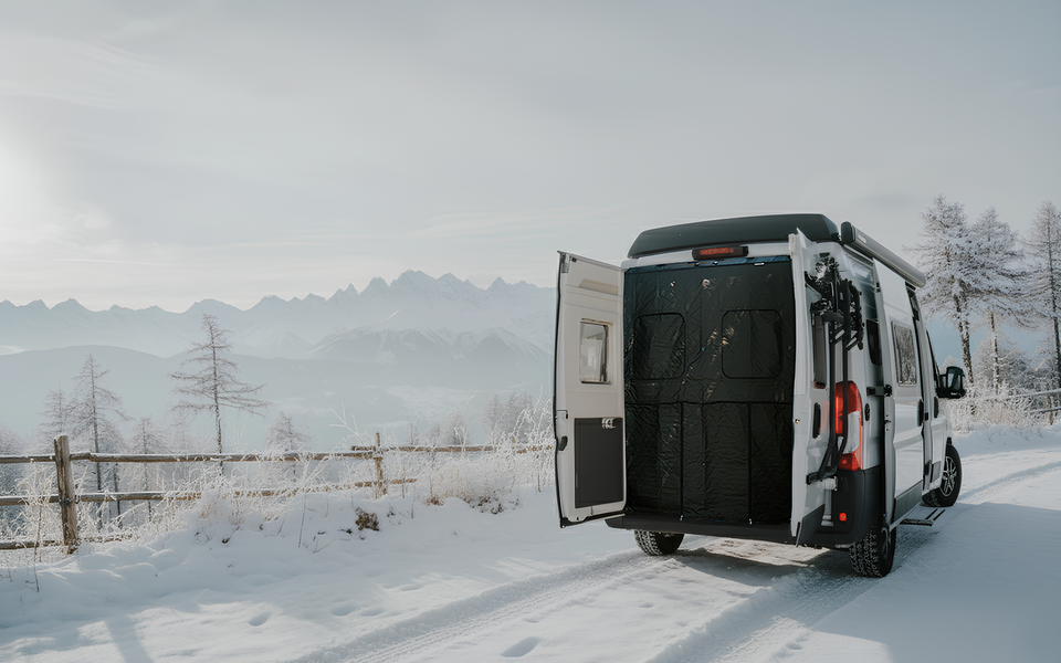 Carado motorhome with rear doors open on a snow-covered road, set against a mountain panorama