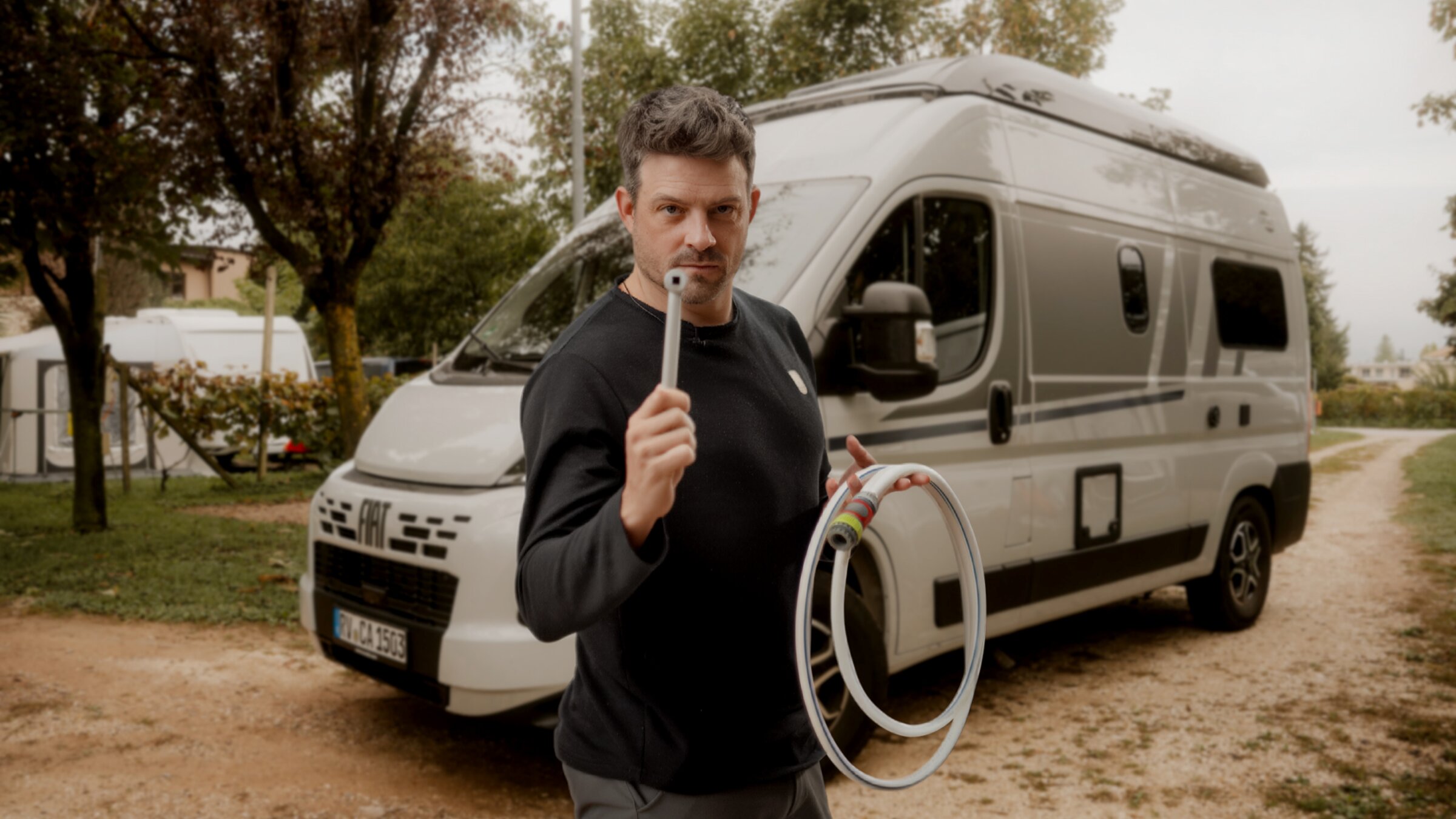 Mann steht mit einem sauberen Wasserschlauch und Adapter zum Befüllen des Wassertanks vor einem Wohnmobil