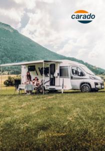 Carado motorhome with awning, table and two people on a meadow in front of a mountain backdrop