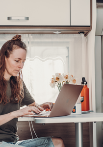 Frau arbeitet mit Laptop am Tisch im Innenraum eines Carado Wohnmobils