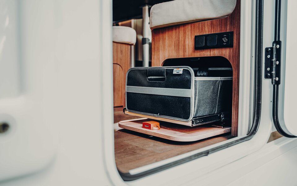 Pull-out storage compartment in the Carado motorhome with black bag under the seat bench at the entrance
