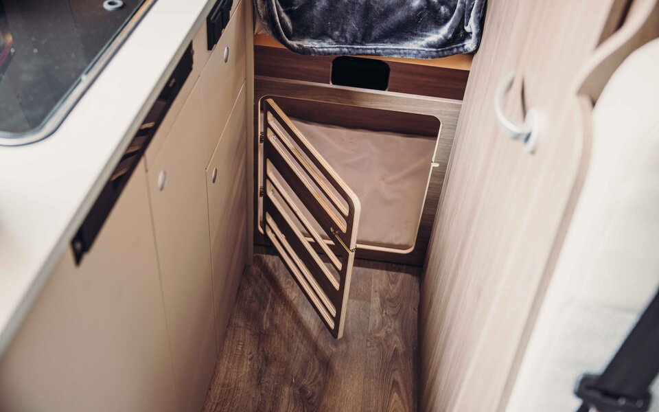Carado motorhome interior with open storage hatch and laundry compartment next to the kitchenette
