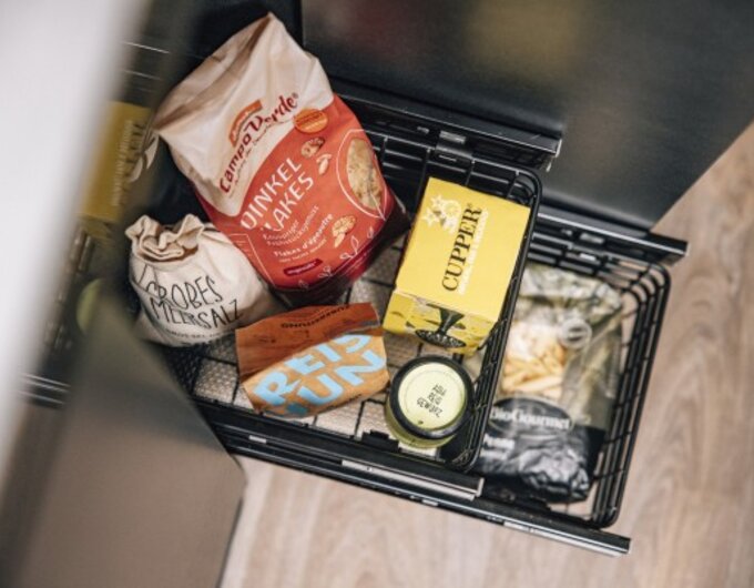 Pull-out pantry cabinet in the Carado motorhome, stocked with food such as biscuits, soup packets and jars