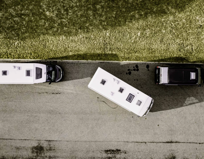 Top view of two Carado motorhomes and a camper van on asphalt beside a meadow