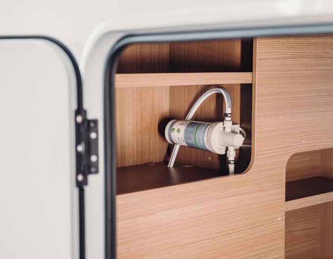 Water filter in the open wooden compartment of a Carado motorhome, with hoses visible