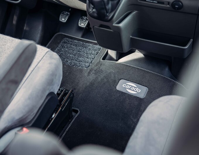 Driver's cab footwell of a Carado motorhome with pedals and Carado floor mat