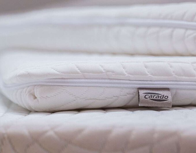 Close-up of stacked white Carado mattress toppers with zipper and logo label