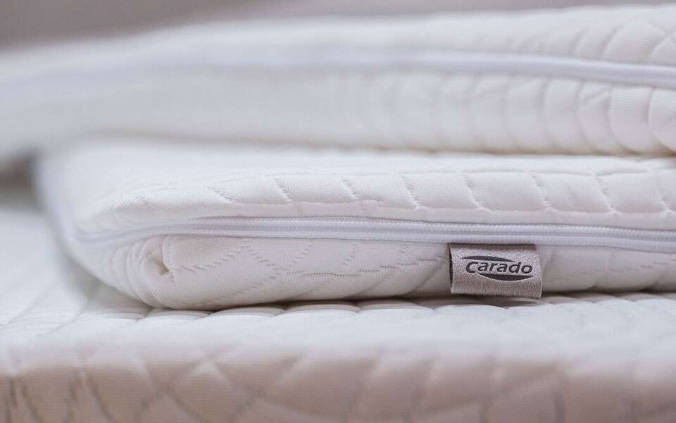 Close-up of stacked white Carado mattress toppers with zipper and logo label