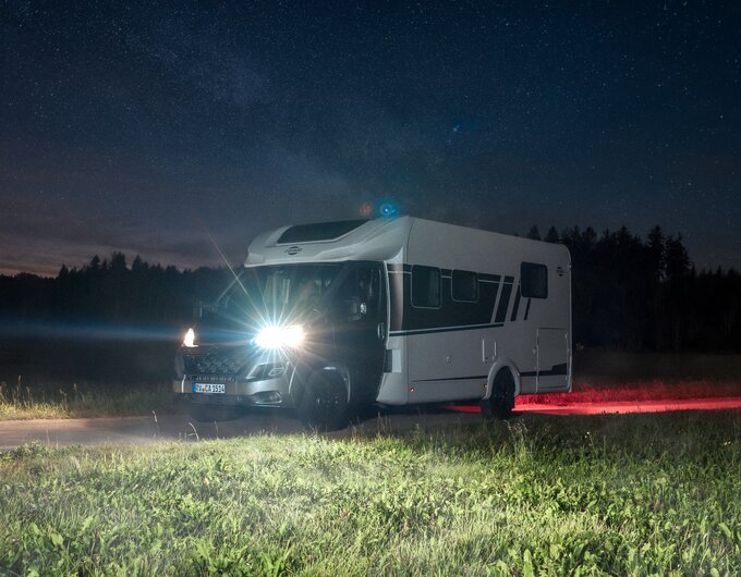 Camping-car Carado de nuit sur un chemin de campagne, feux allumés sous un ciel étoilé