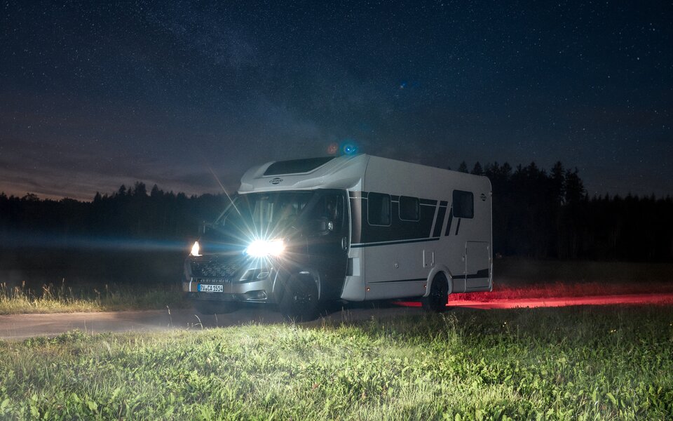 Carado motorhome at night on a country lane with the lights on under a starry sky