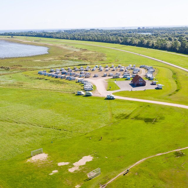 Aerial view of a motorhome pitch on the coast, with many campers, meadows, paths and a small building