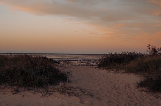 A sandy path between the dunes to the beach and the Wadden Sea at dusk