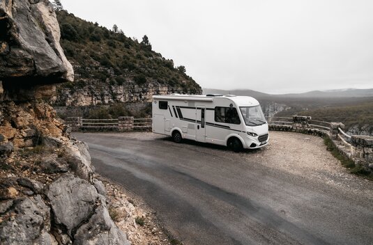 Camping-car Carado sur une route en lacets le long d'une paroi rocheuse, avec vue sur la vallée