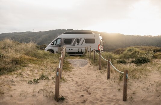 Camping-car Carado sur un chemin de sable entre les dunes, vue de côté dans la lumière basse du soleil