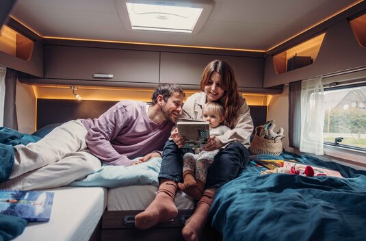 Family with a toddler reading in the rear bed of a Carado motorhome