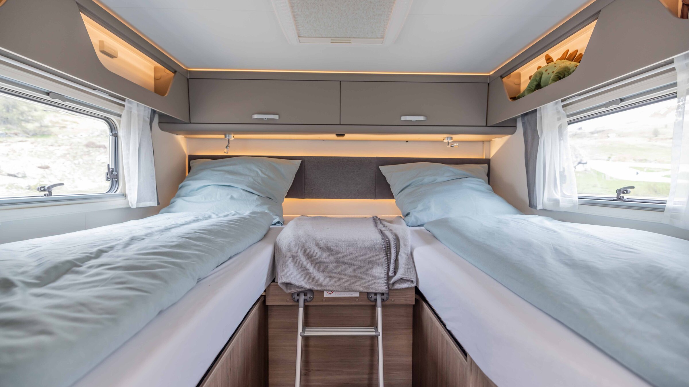 Slaapgedeelte in de Carado camper met twee eenpersoonsbedden, ladder, bovenkasten en zijramen
