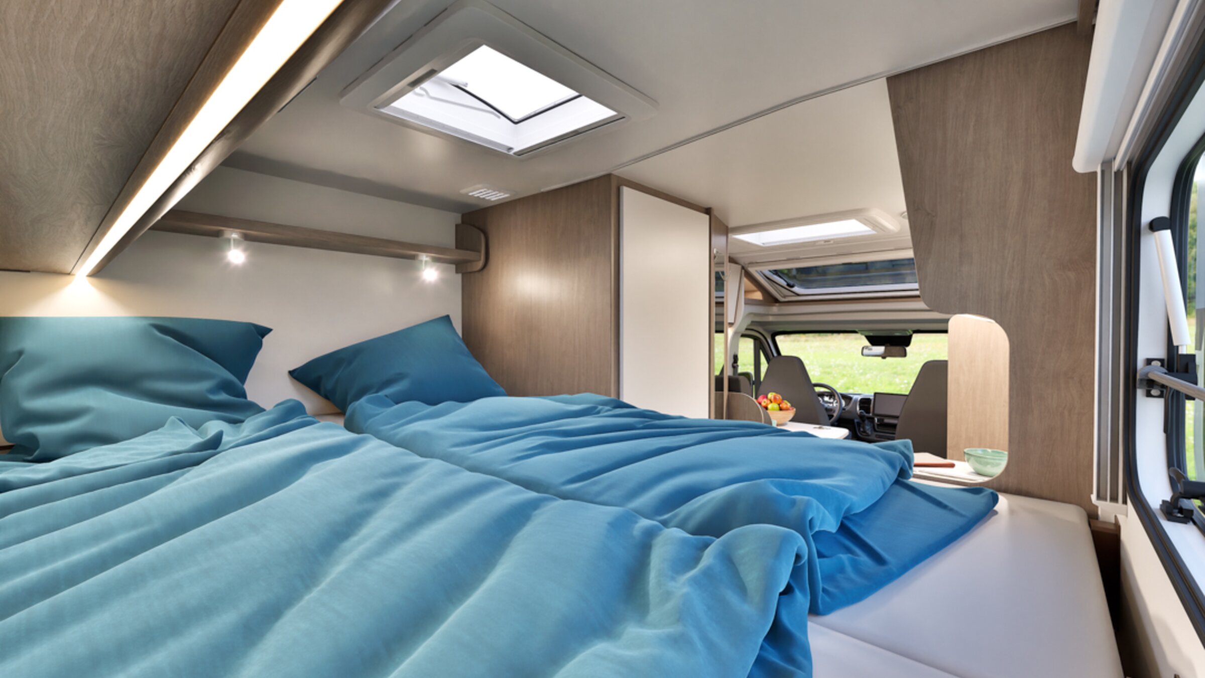 Slaap lekker onderweg: slaapgedeelte in de Carado camper met tweepersoonsbed, blauw beddengoed, dakraam en uitzicht naar voren op de bestuurderscabine