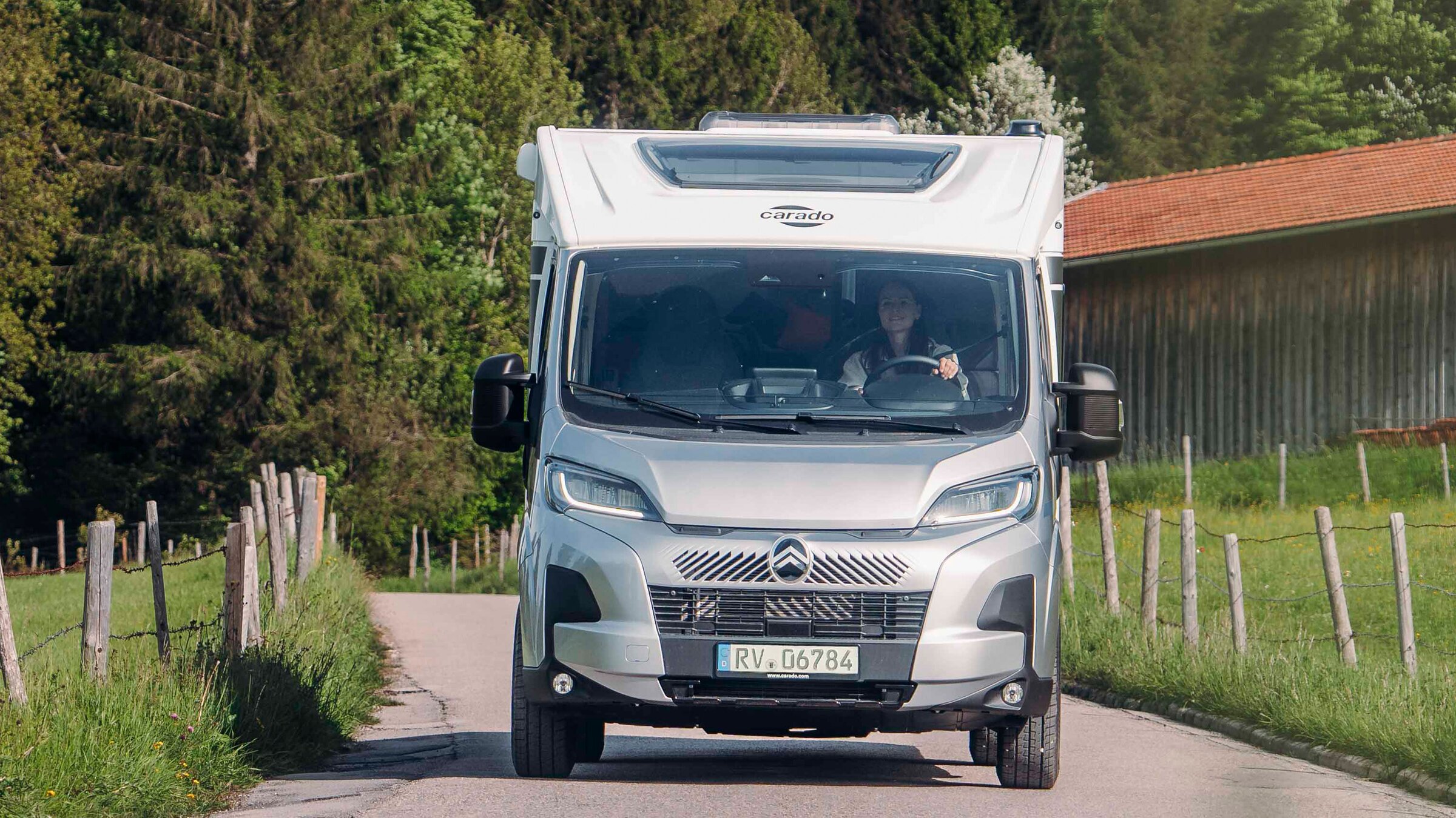 Carado motorhome, front view, on a narrow country road in front of a wooded slope