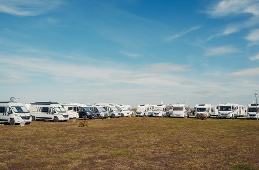 Several motorhomes and camper vans parked on an open pitch under a blue sky