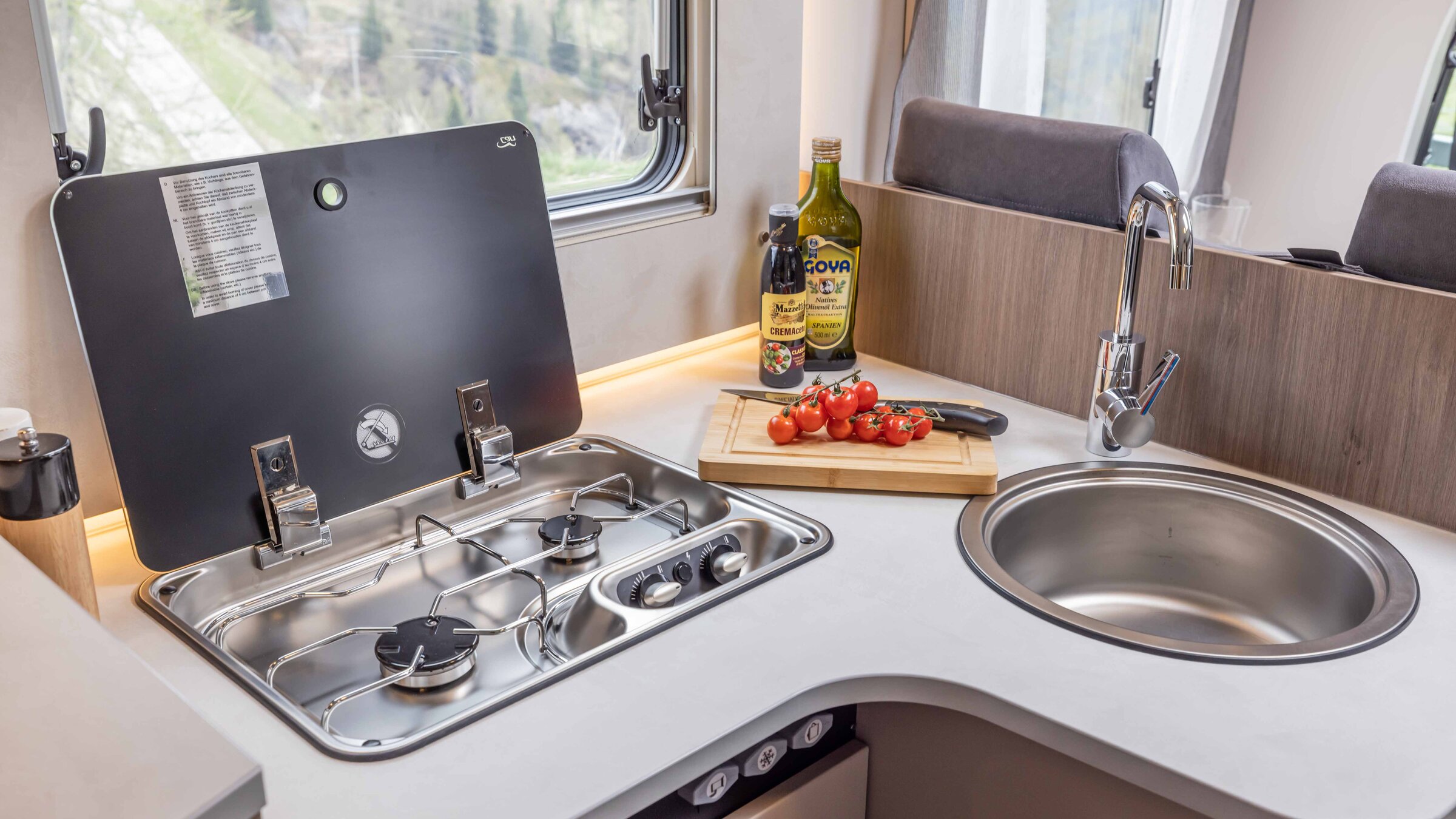 Carado motorhome kitchen with two-burner gas hob, round sink and worktop with tomatoes and oil