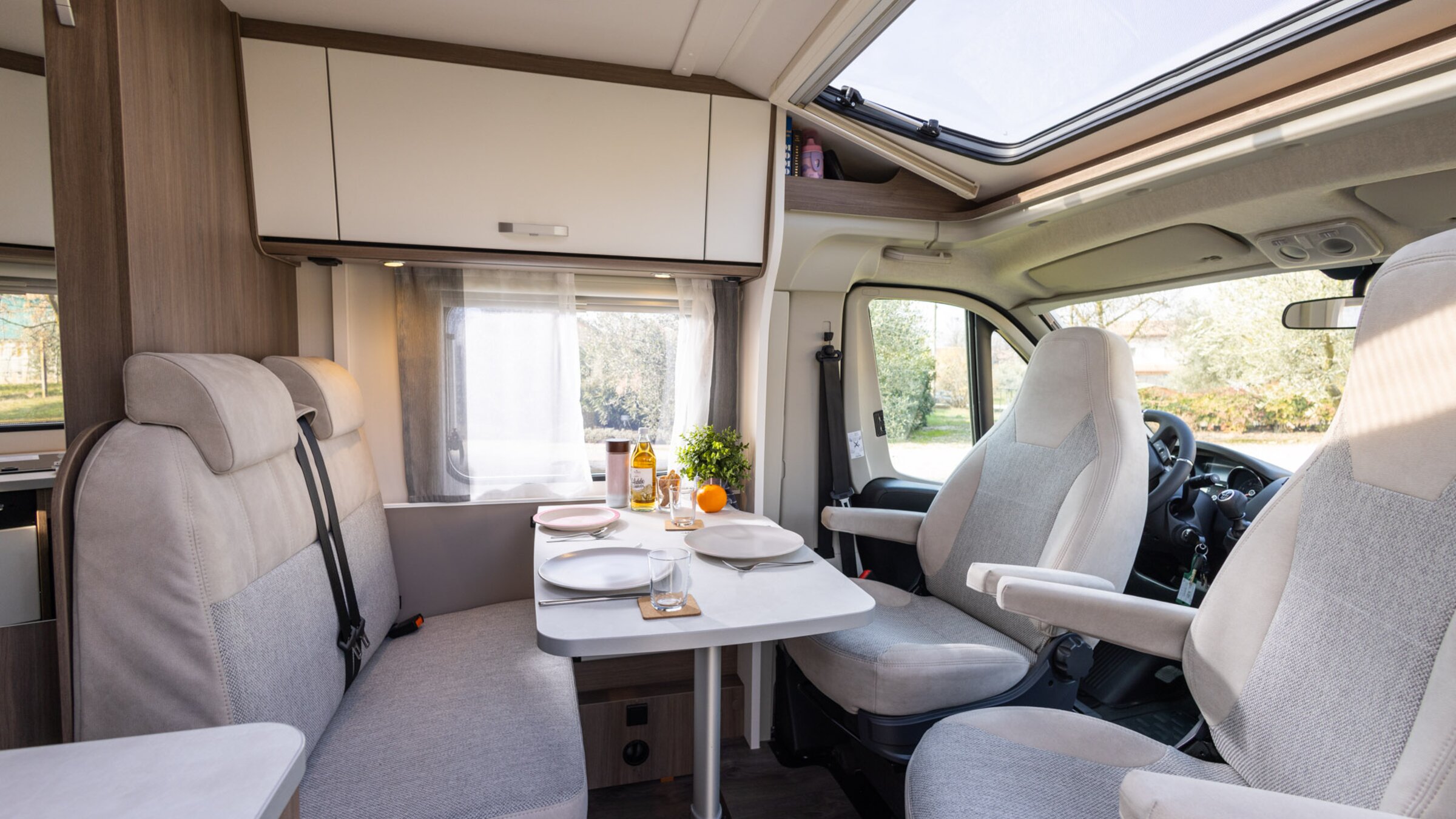 Intérieur du camping-car Carado avec coin salon, sièges de cabine pivotants, table et lanterneau