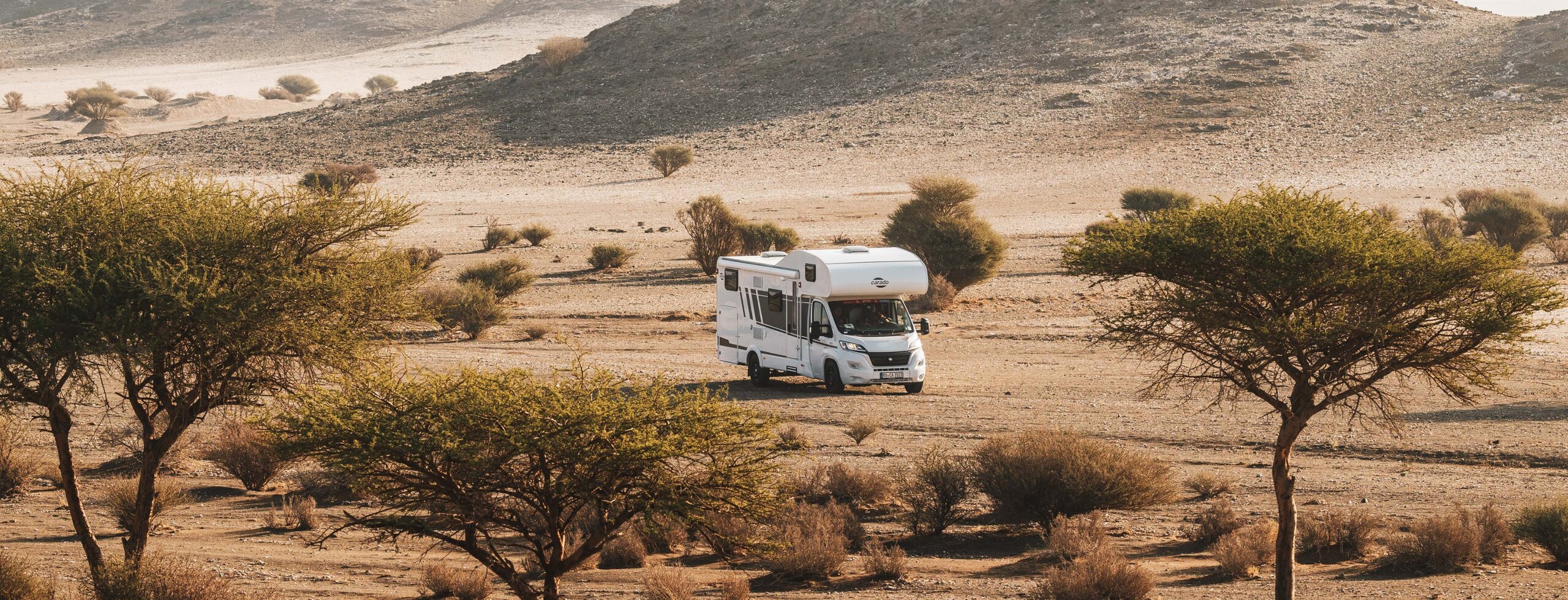 Carado motorhome in a sparse desert landscape with trees and rocky hills